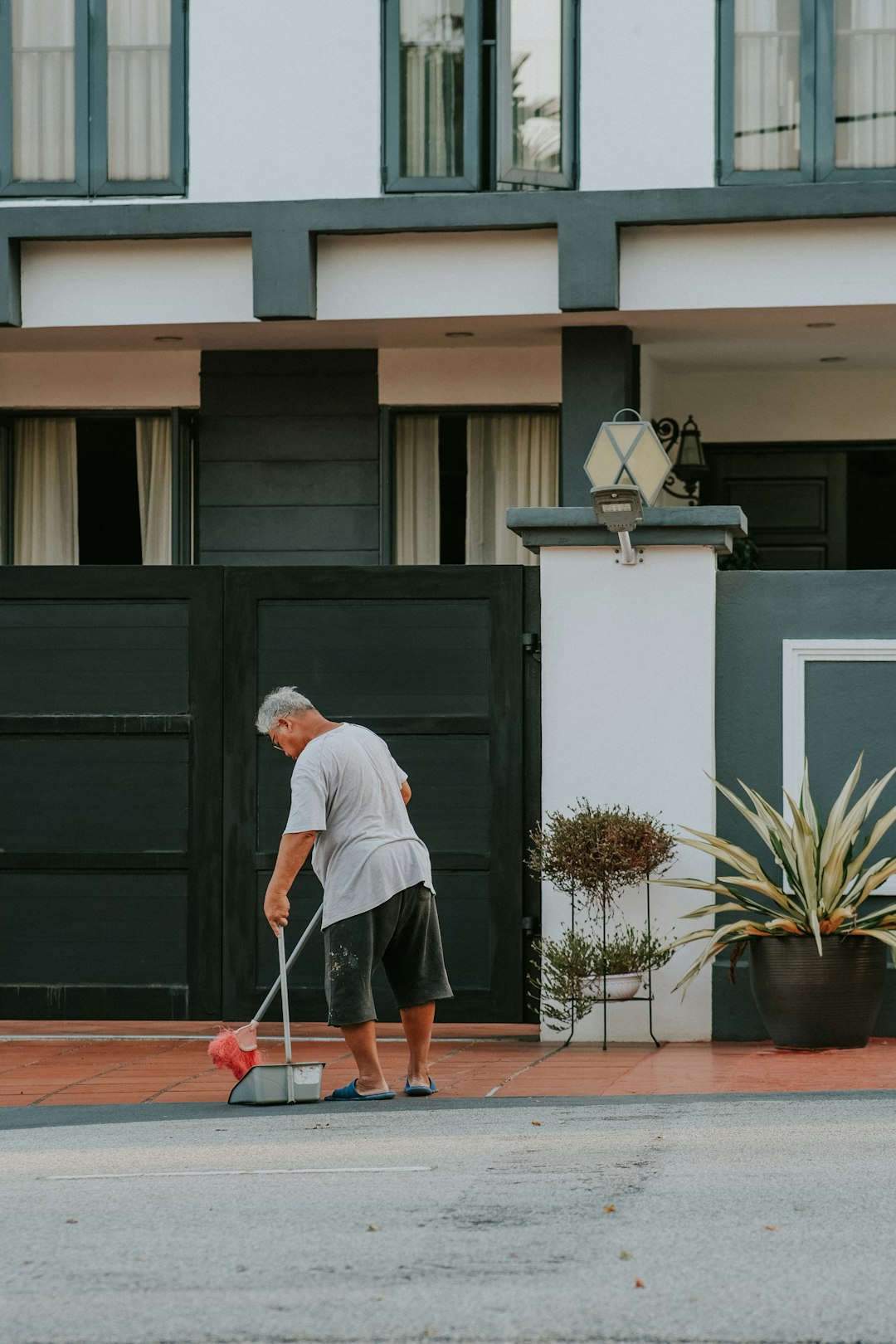 Chinese elderly man sweeping in front of a house gate.