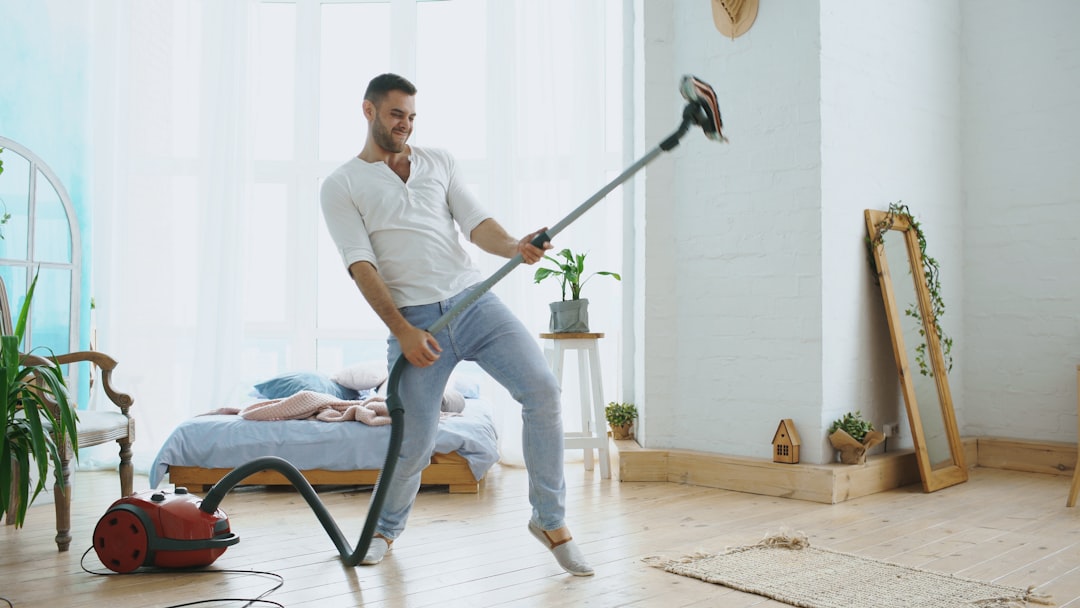 Dancing young man having fun cleaning house with vacuum cleaner at home